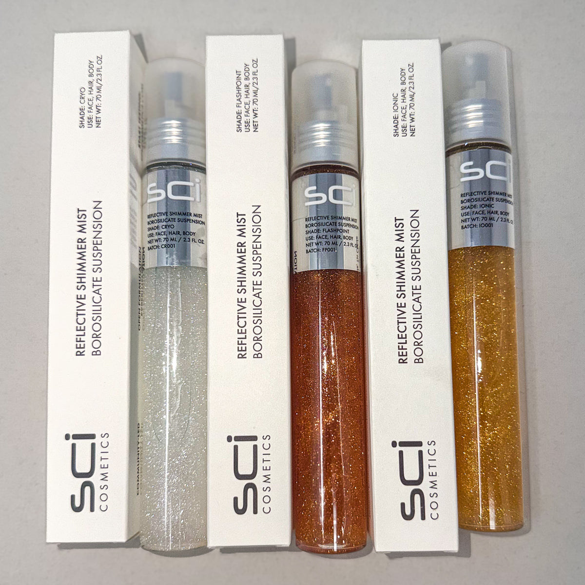 Four SCI Cosmetics Reflective Shimmer Mist bottles with their white packaging boxes, arranged side-by-side on a neutral gray background. The bottles contain shimmering suspensions in silver, bronze, and gold shades.